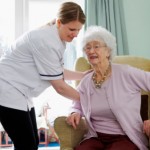 carer helps her elderly pacient to her feet from her chair